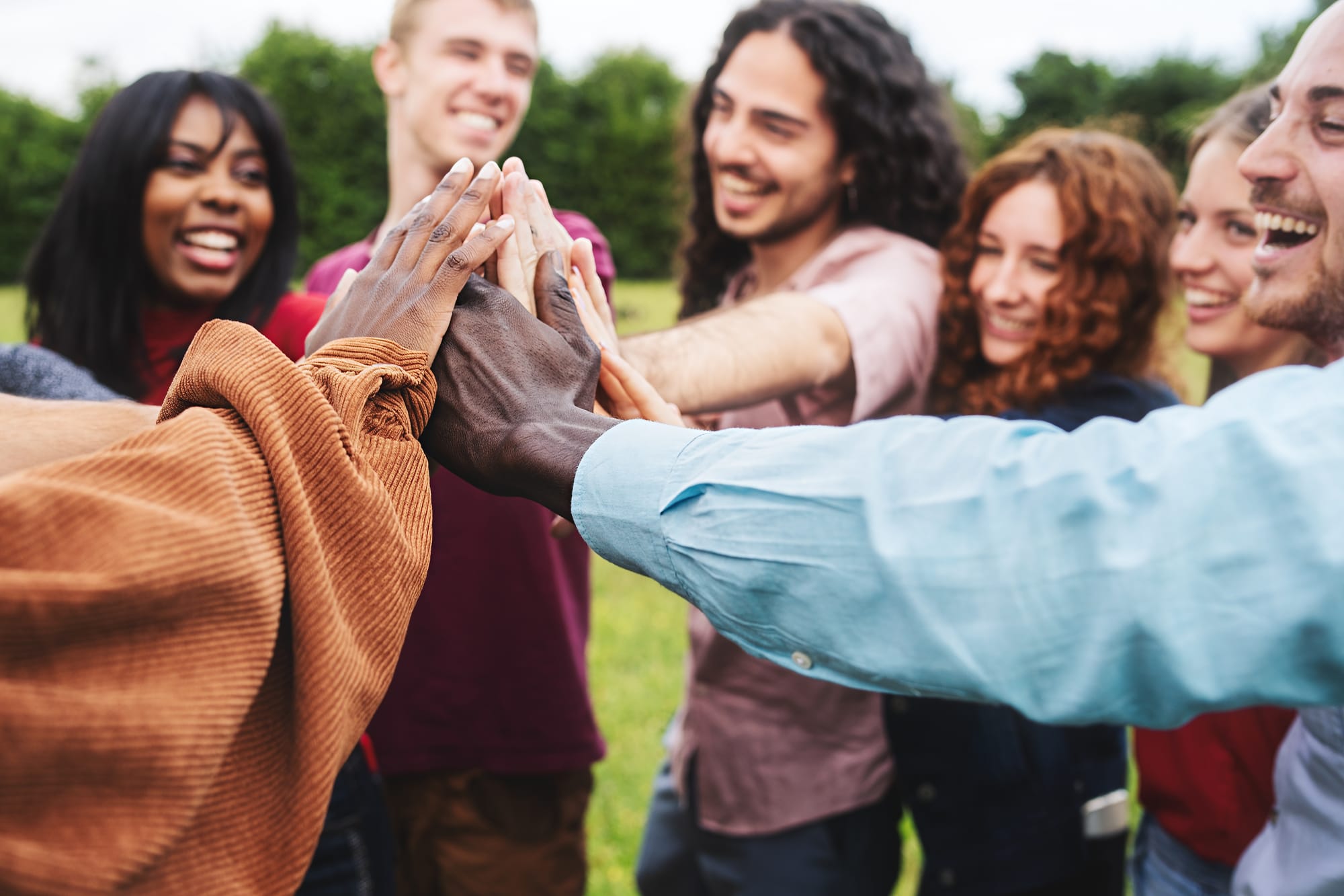 Groupe diversifié de personnes souriantes, mains réunies au centre